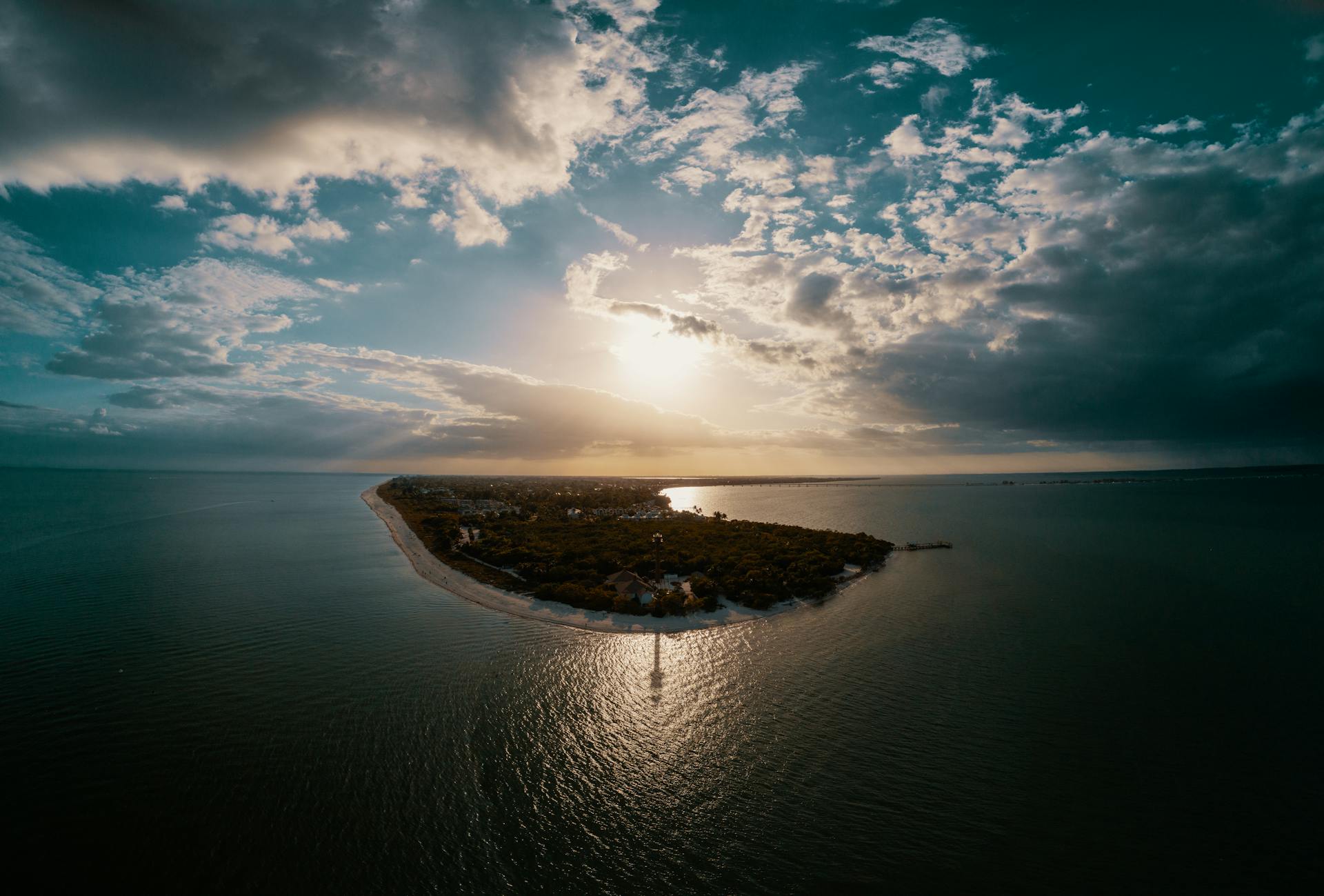 A serene aerial shot capturing an island at sunset with dramatic clouds and calm sea.