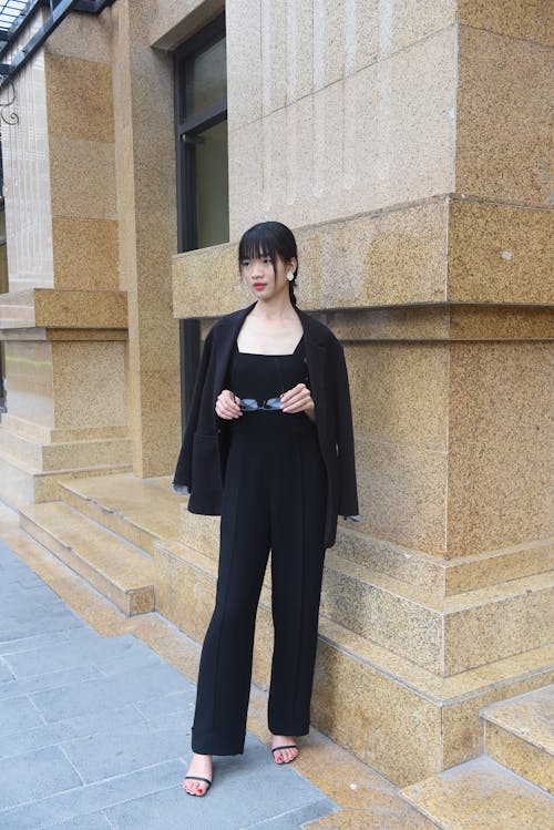 A woman in a black jumpsuit standing on a sidewalk