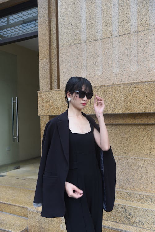 A woman in a black suit and sunglasses standing on a sidewalk