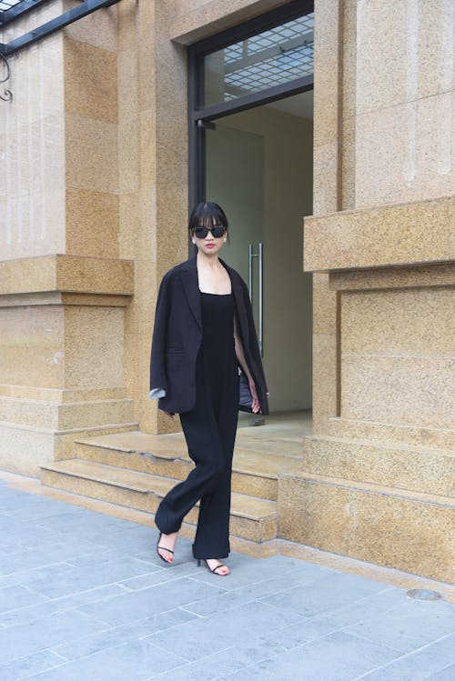 A woman in black suit and sunglasses walking down the street