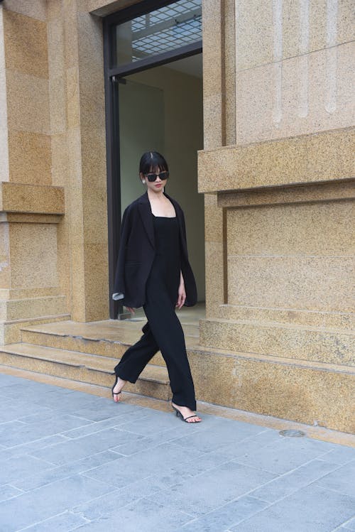 A woman in a black jumpsuit walking down a sidewalk