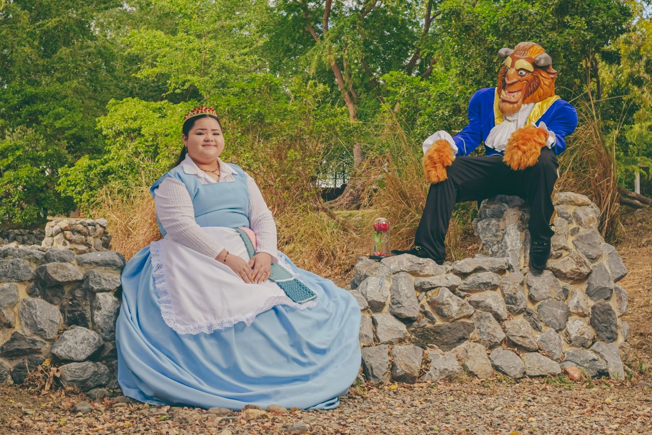 a woman in a blue dress and a beast costume outdoors evoking a fairy t