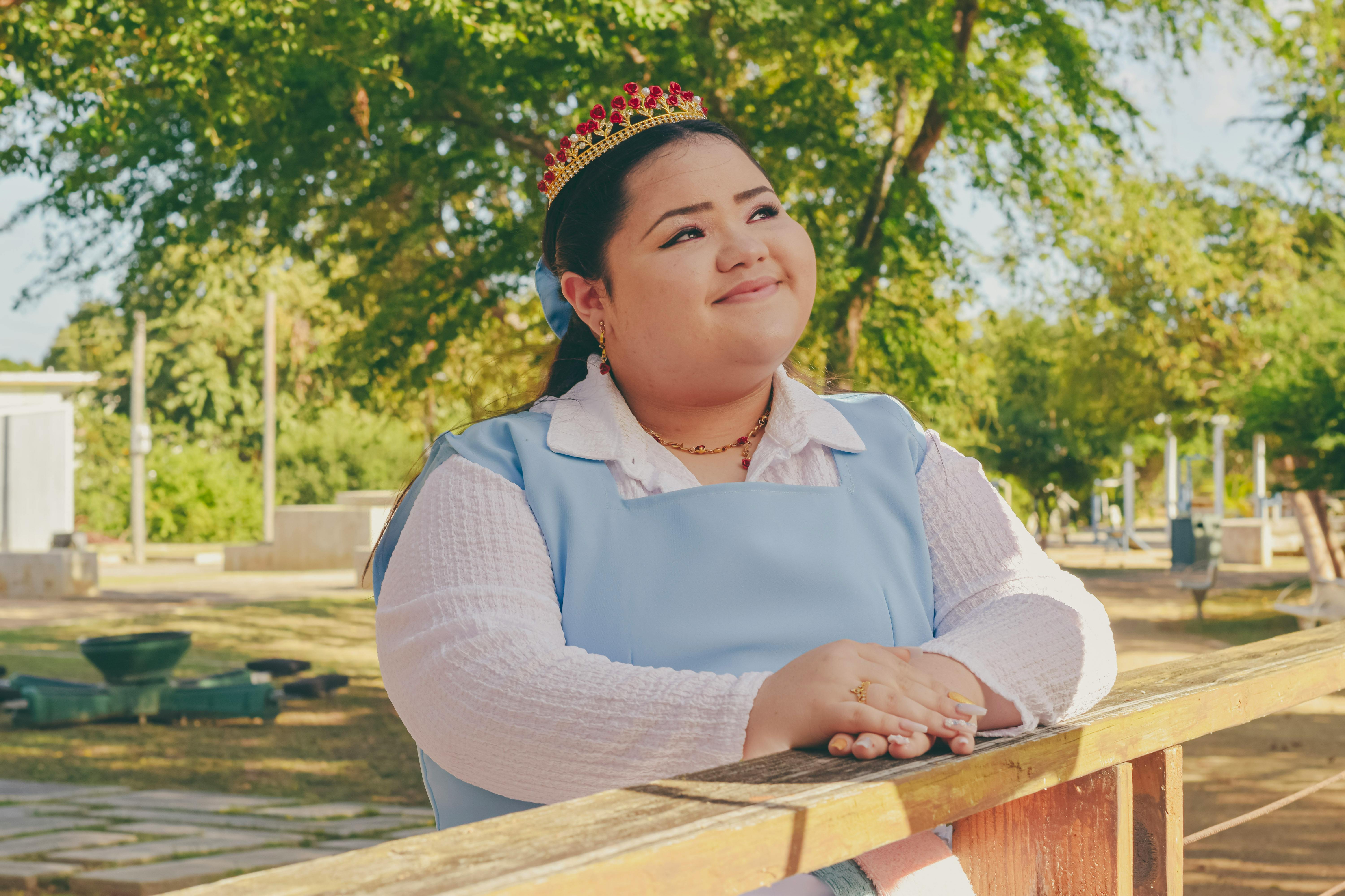 A woman in a blue dress and a crown is standing on a wooden fence