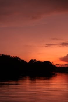 Beautiful sunset view with vibrant orange sky reflecting over a calm lake for a perfect evening atmosphere.
