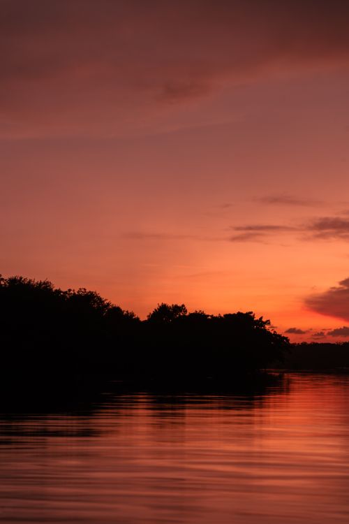 Free Beautiful sunset view with vibrant orange sky reflecting over a calm lake for a perfect evening atmosphere. Stock Photo