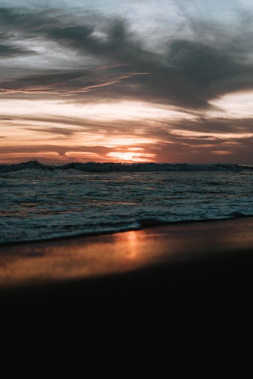 Free A mesmerizing sunset over ocean waves with dramatic clouds creating a vivid seascape. Stock Photo