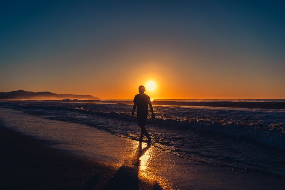 A silhouette of a person walking along the shore with a vibrant sunset in the background, reflecting on the water.