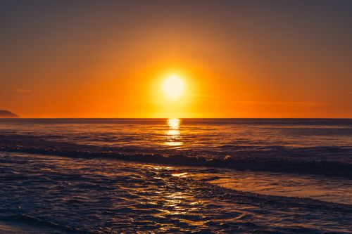 Free Stunning sunset over ocean waves with vibrant orange hues reflecting on the water's surface. Stock Photo
