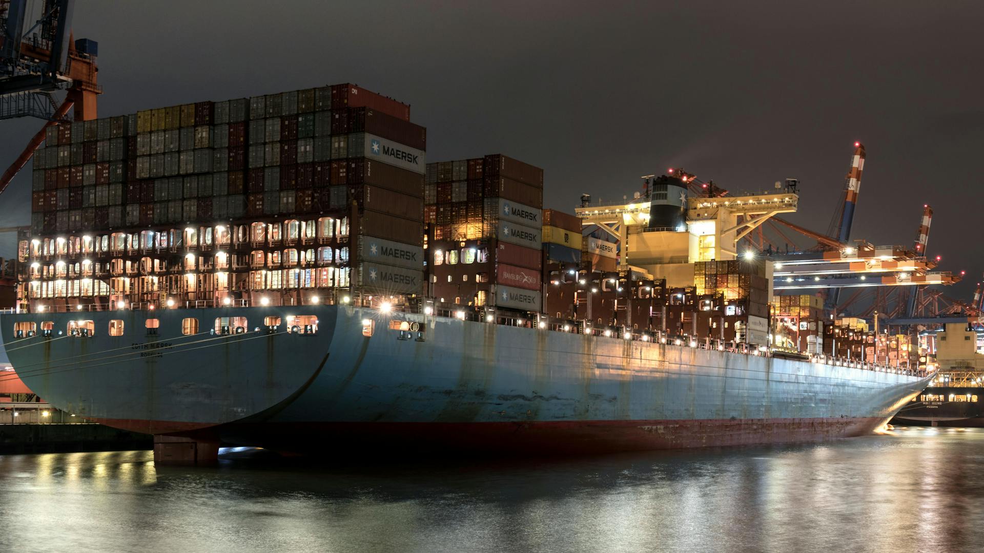 Night view of a cargo ship loaded with containers at Hamburg port, showcasing logistics and trade.