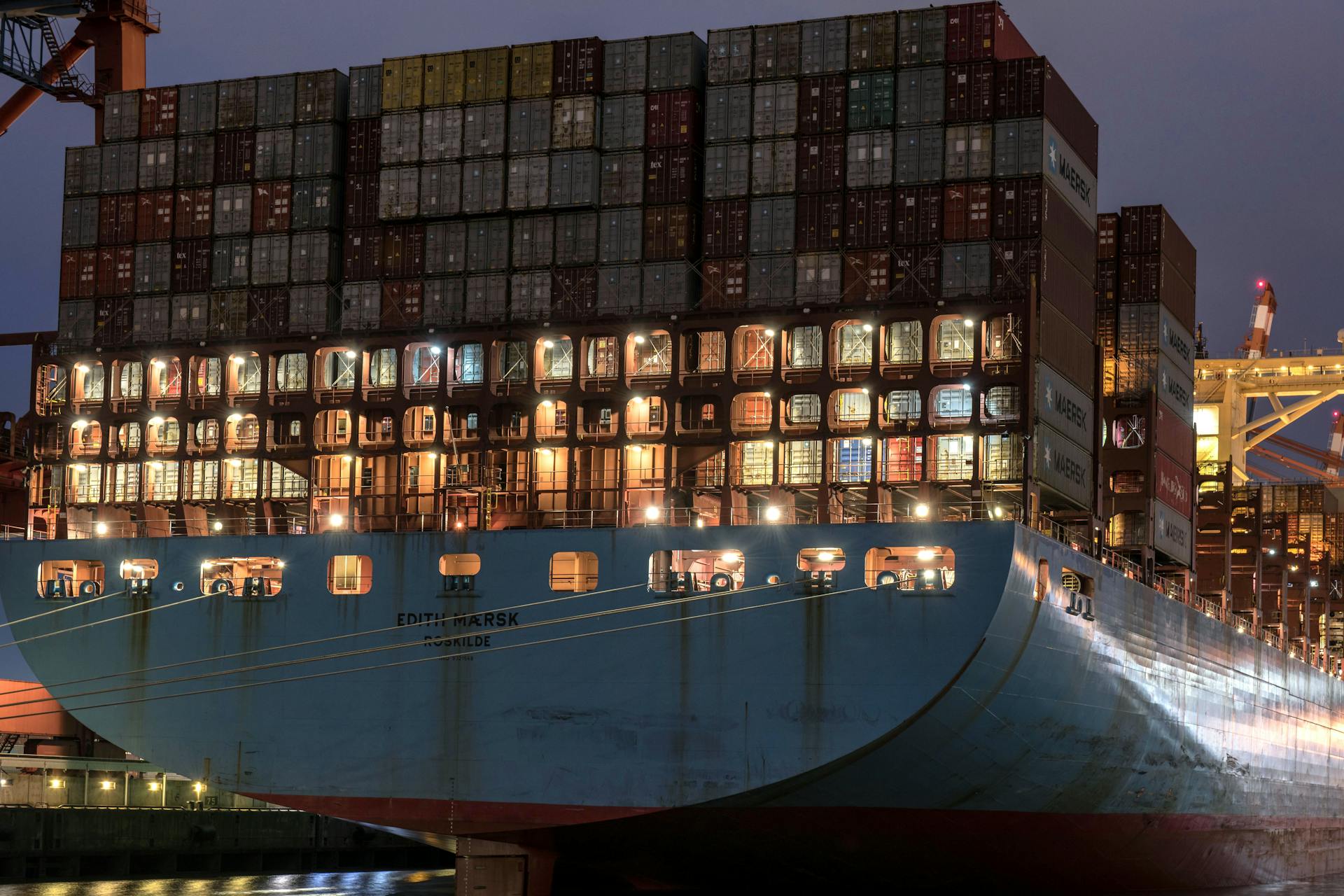 Large container ship Edith Maersk docked at Hamburg harbor during evening lights.