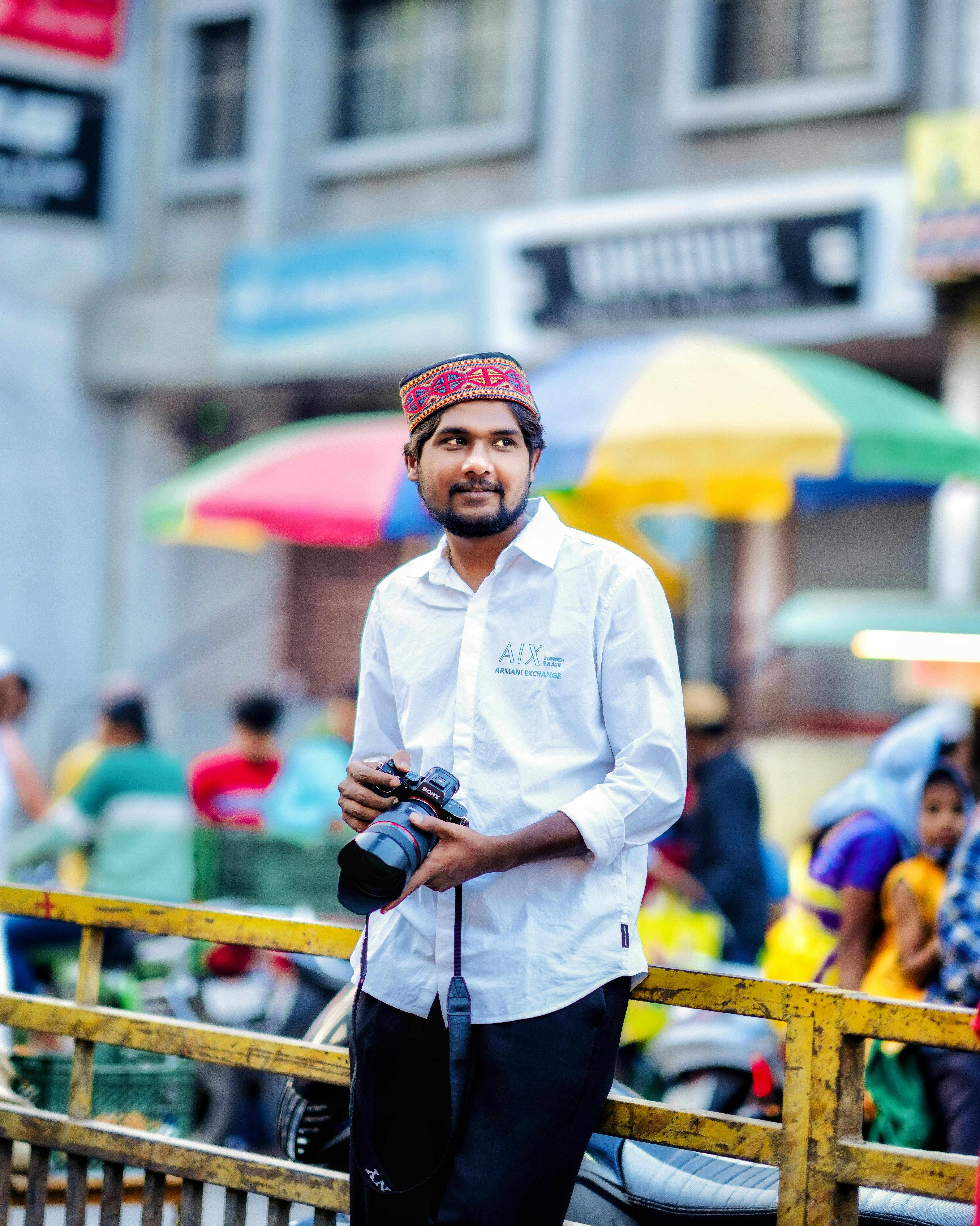 South Asian male photographer in traditional clothing with colorful urban backdrop.