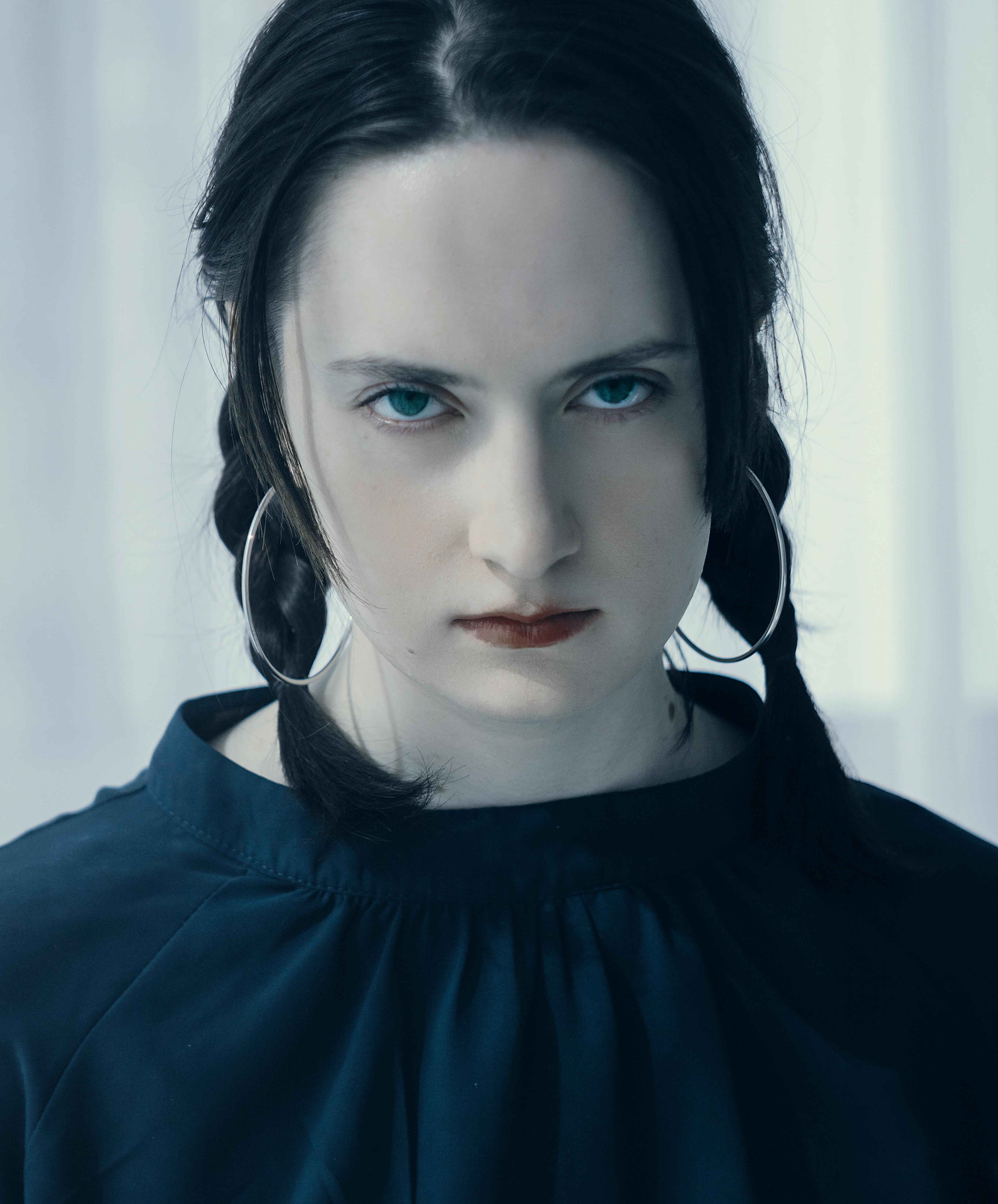 Intense portrait of a young woman with braids and hoop earrings, captured in soft lighting.