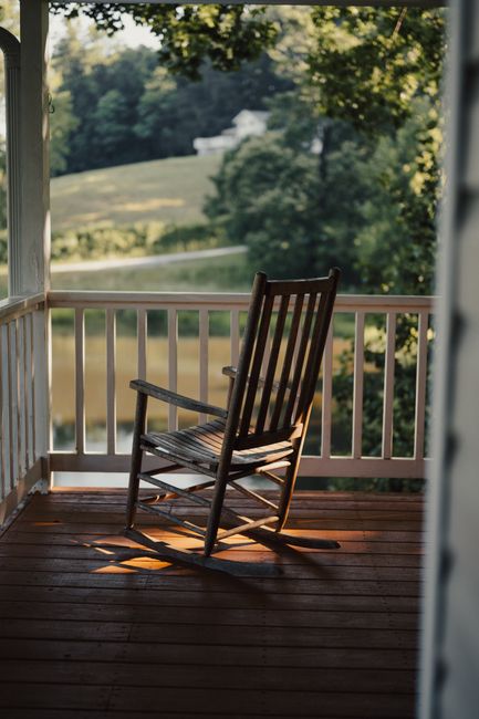 A serene countryside view from a porch with a wooden rocking chair, ideal for relaxation.