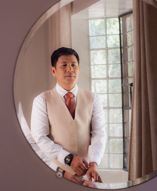 A man in a vest and tie standing in front of a mirror