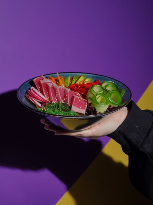 A person holding a bowl of food with vegetables and meat