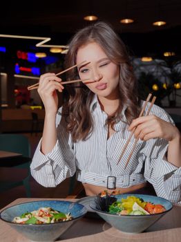 Woman playfully posing with chopsticks in a modern restaurant, enjoying a meal.