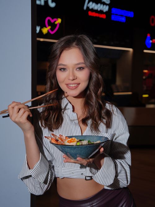 Free Smiling woman with long brown hair holding seafood bowl using chopsticks indoors at night. Stock Photo
