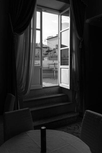 A sophisticated black and white image of an open door leading to a terrace, captured from within a stylish room.