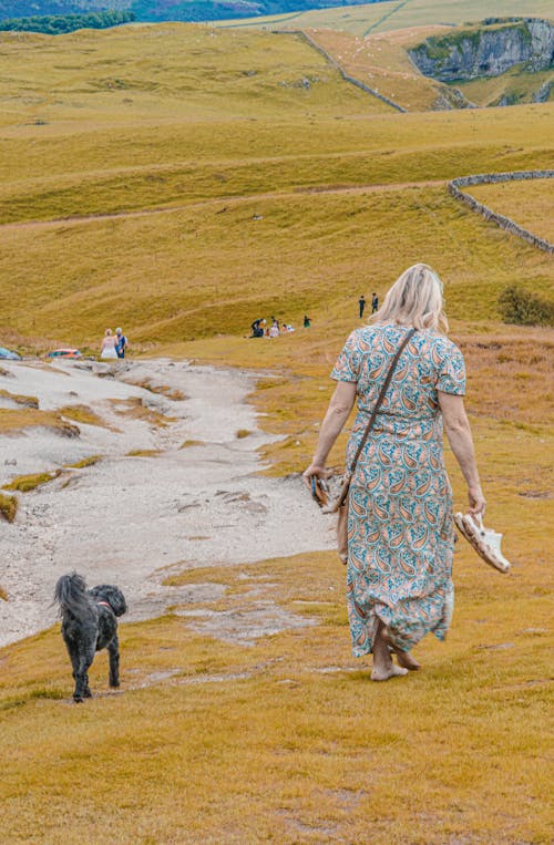 Woman in Sundress Walking Barefoot with Dog on Grassland