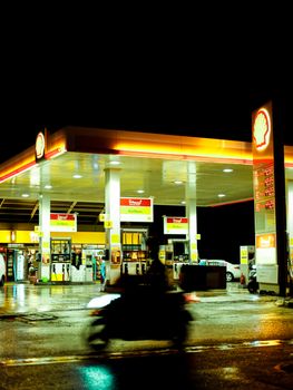Photo by Esra Korkmaz Blurred motor scooter passing by an illuminated Shell gas station during night time with signage visible.