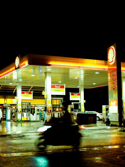 Free Blurred motor scooter passing by an illuminated Shell gas station during night time with signage visible. Stock Photo