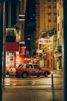 Vibrant Hong Kong street at night with a classic red taxi and urban sights.