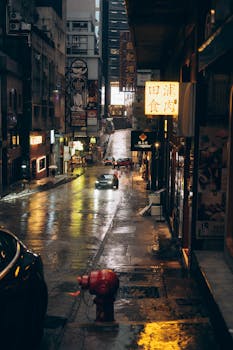 Rain-soaked street in Hong Kong at night, capturing urban life with neon lights and reflections.