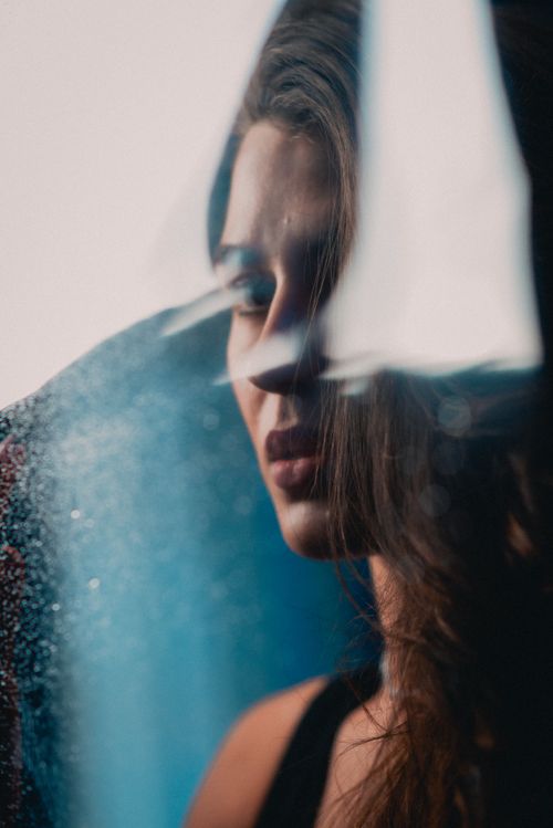 Free Captivating portrait of a woman with long brown hair viewed through a rainy window, evoking emotion and introspection. Stock Photo