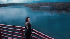 一名女子身穿黑色连衣裙，站在红色栏杆上，俯瞰着宁静的河流