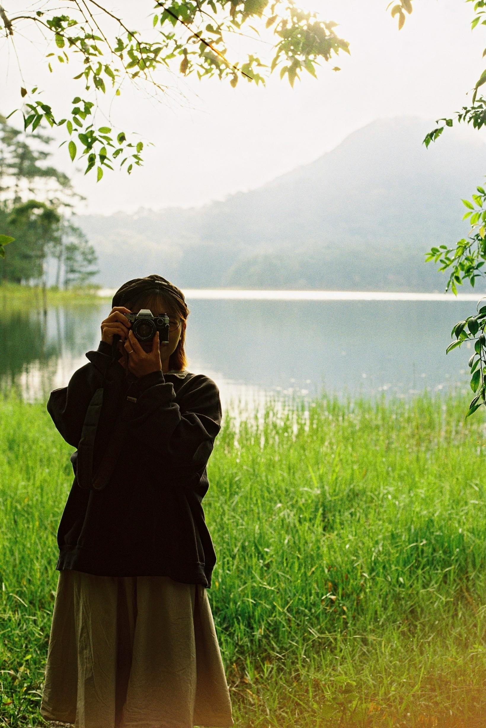 Woman photographer by a serene lake during a calm day in the countryside.