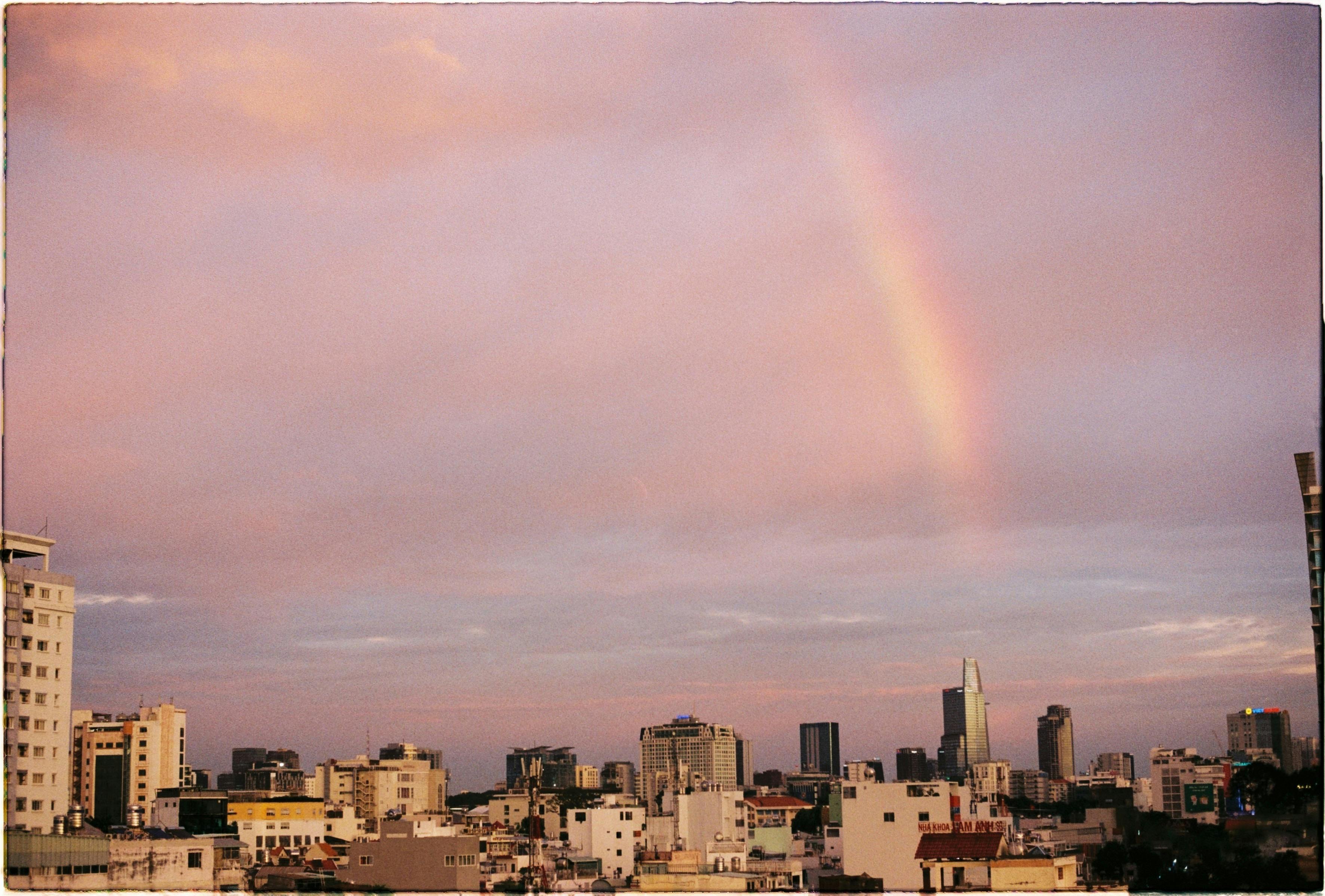 A stunning rainbow arches over a bustling city skyline during a serene dusk.