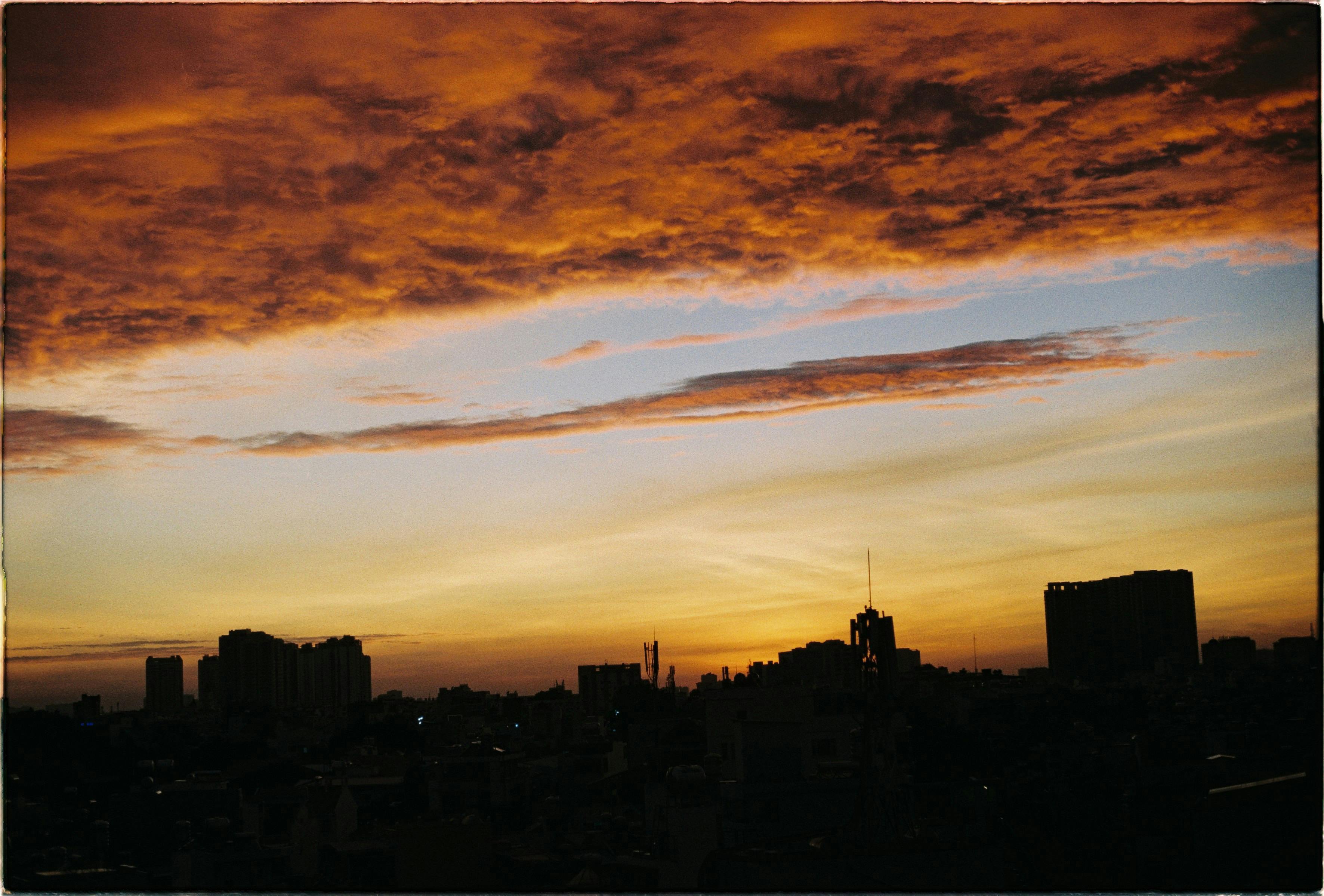 Dramatic sunset over city skyline with vibrant clouds and silhouettes of buildings.