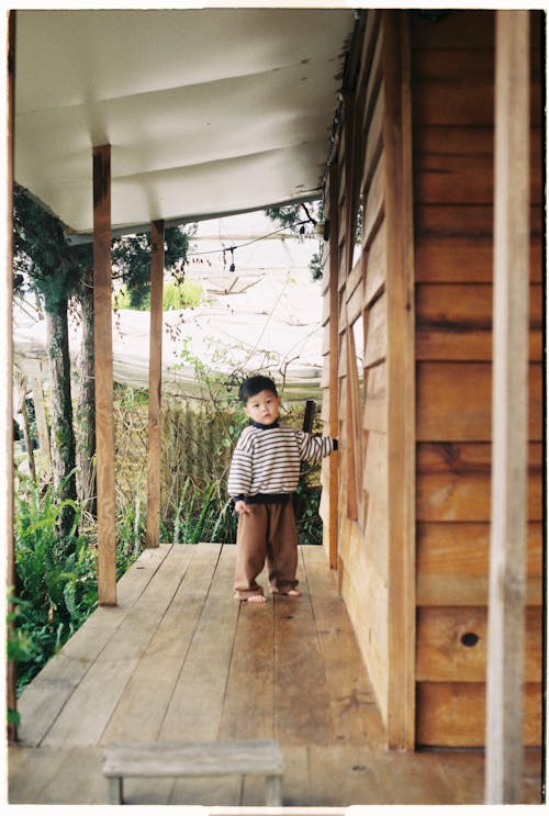 A child standing on the porch of a wooden house