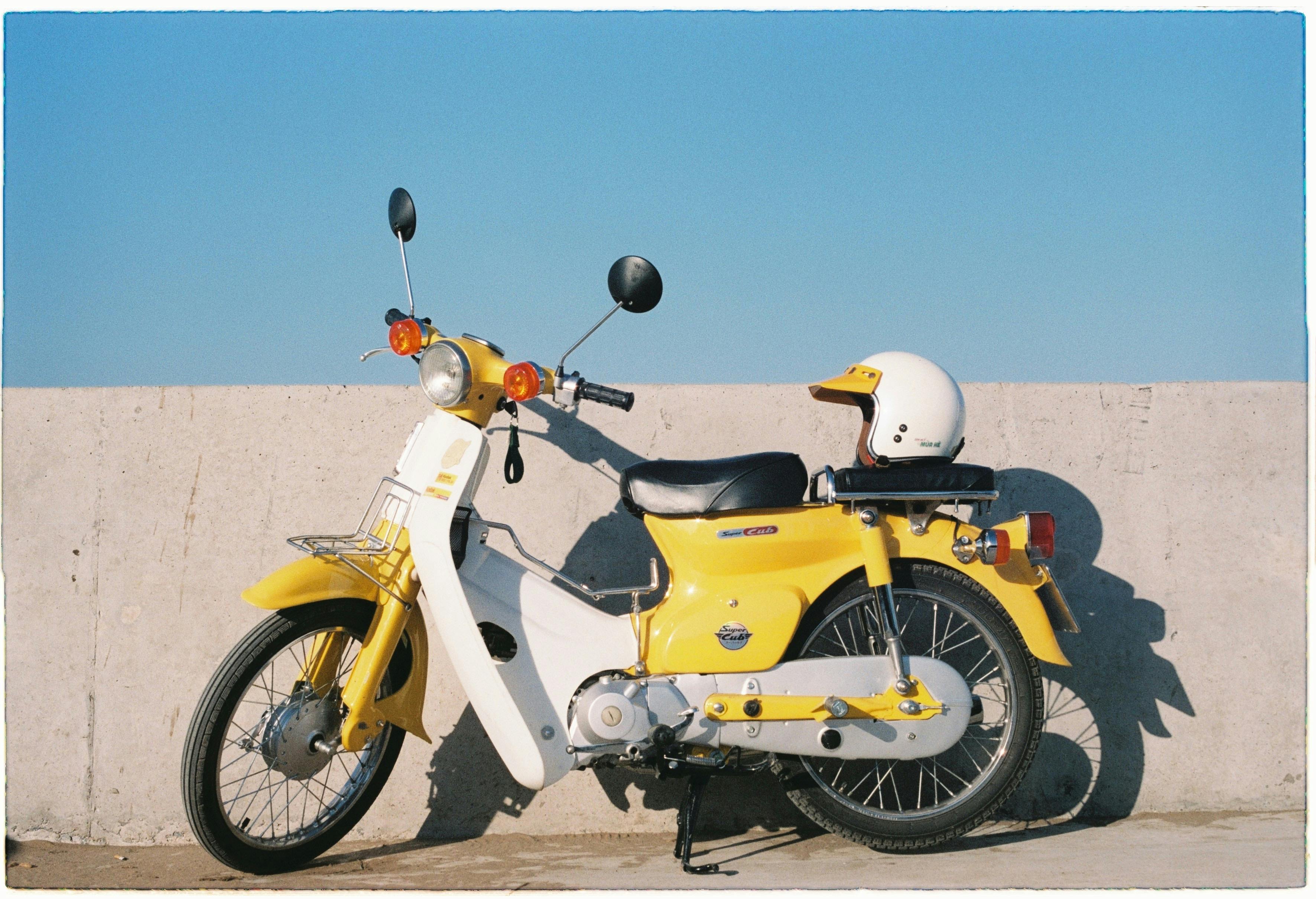 Yellow vintage motorbike with helmet against a concrete wall under clear blue sky.
