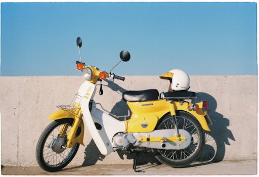 Yellow vintage motorbike with helmet against a concrete wall under clear blue sky.