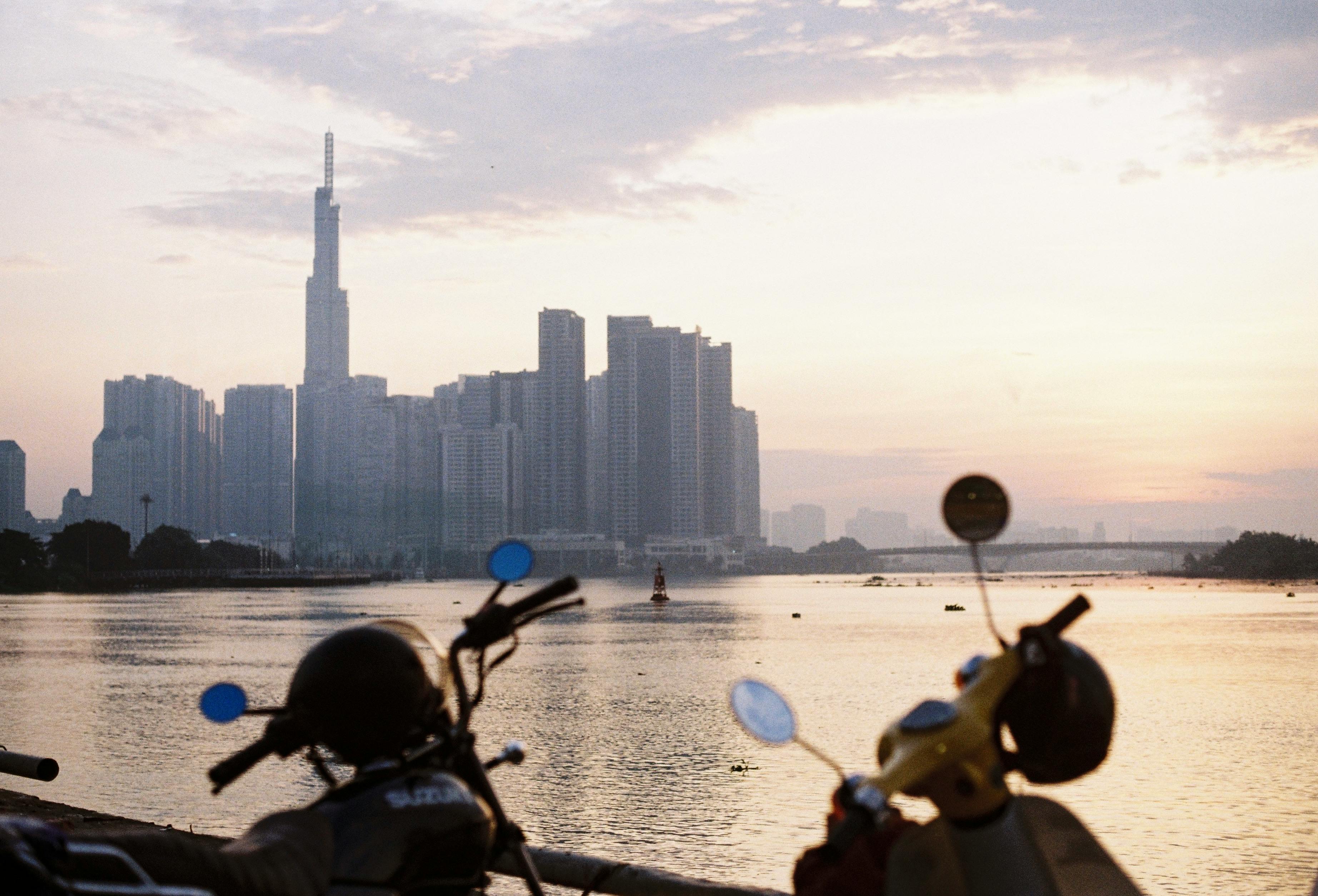 A stunning view of Ho Chi Minh City skyline at sunset with motorbikes in the foreground, capturing urban life.
