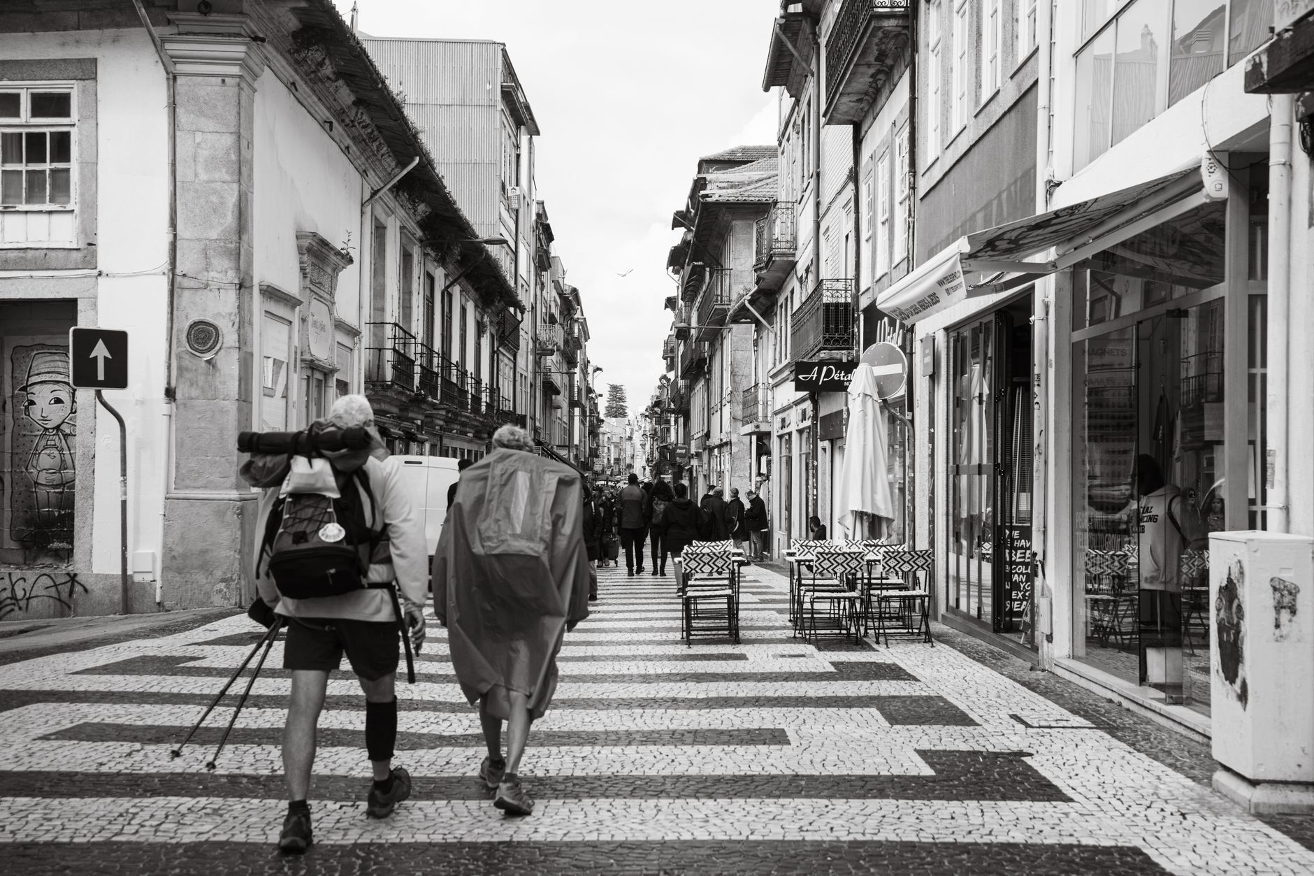 Black and white photo of tourists backpacking in a charming Porto street, capturing urban life.