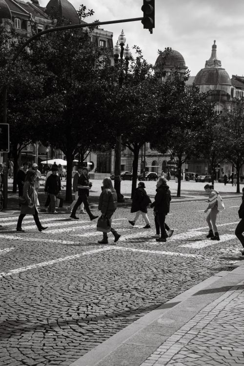 Free Pedestrians crossing a cobblestone street in Porto, Portugal. Captured in black and white, highlighting urban life. Stock Photo