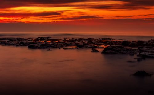 Free Captivating sunset view with a vivid orange sky over a rocky coastline. Stock Photo