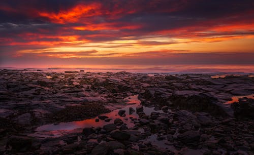 A sunset over a rocky beach with rocks and water