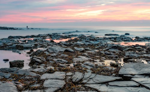 A sunset over rocky shoreline with rocks and water