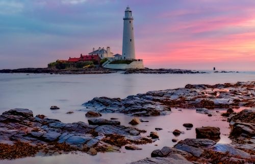 Free Serene sunset view of St Mary's Lighthouse on a rocky coastline, perfect for travel and nature enthusiasts. Stock Photo
