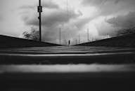 在阴云密布的天空下，一个孤独的身影沿着铁轨前行，构成了一幅充满戏剧性的黑白照片