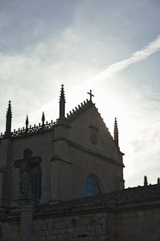 A stunning silhouette of a Gothic church against a sunrise in Burgos, highlighting its spires and cross.