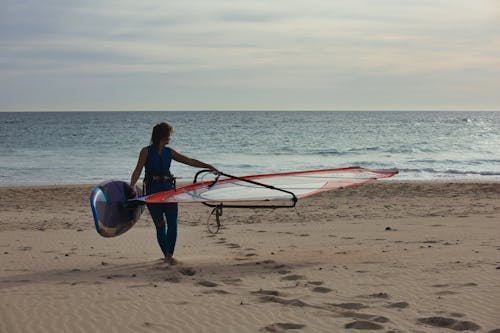 A woman walking on the beach with a windsurfer