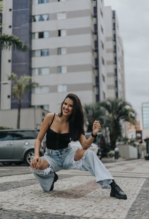 A woman in jeans and a top is posing in front of a building