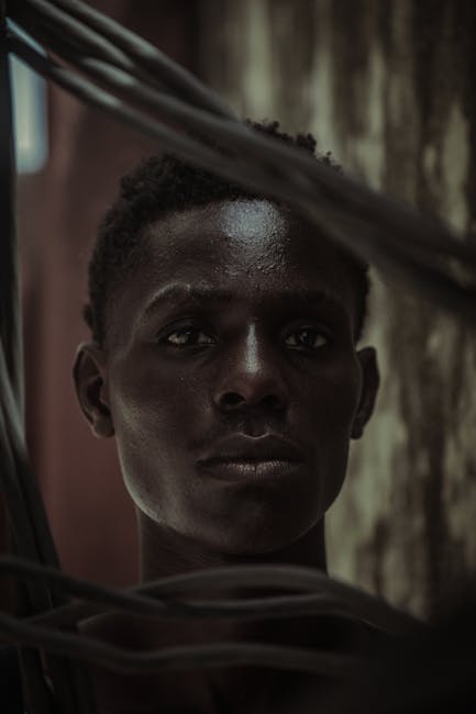 Dramatic portrait of a young man with short hair enveloped in shadows, conveying depth and mystery.