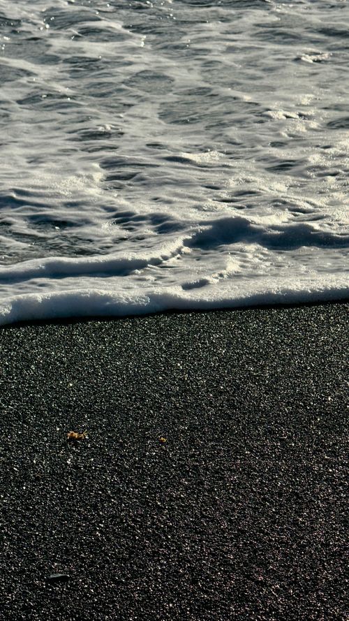 Free Detailed shot of waves lapping a black sand beach, highlighting texture and contrast. Stock Photo