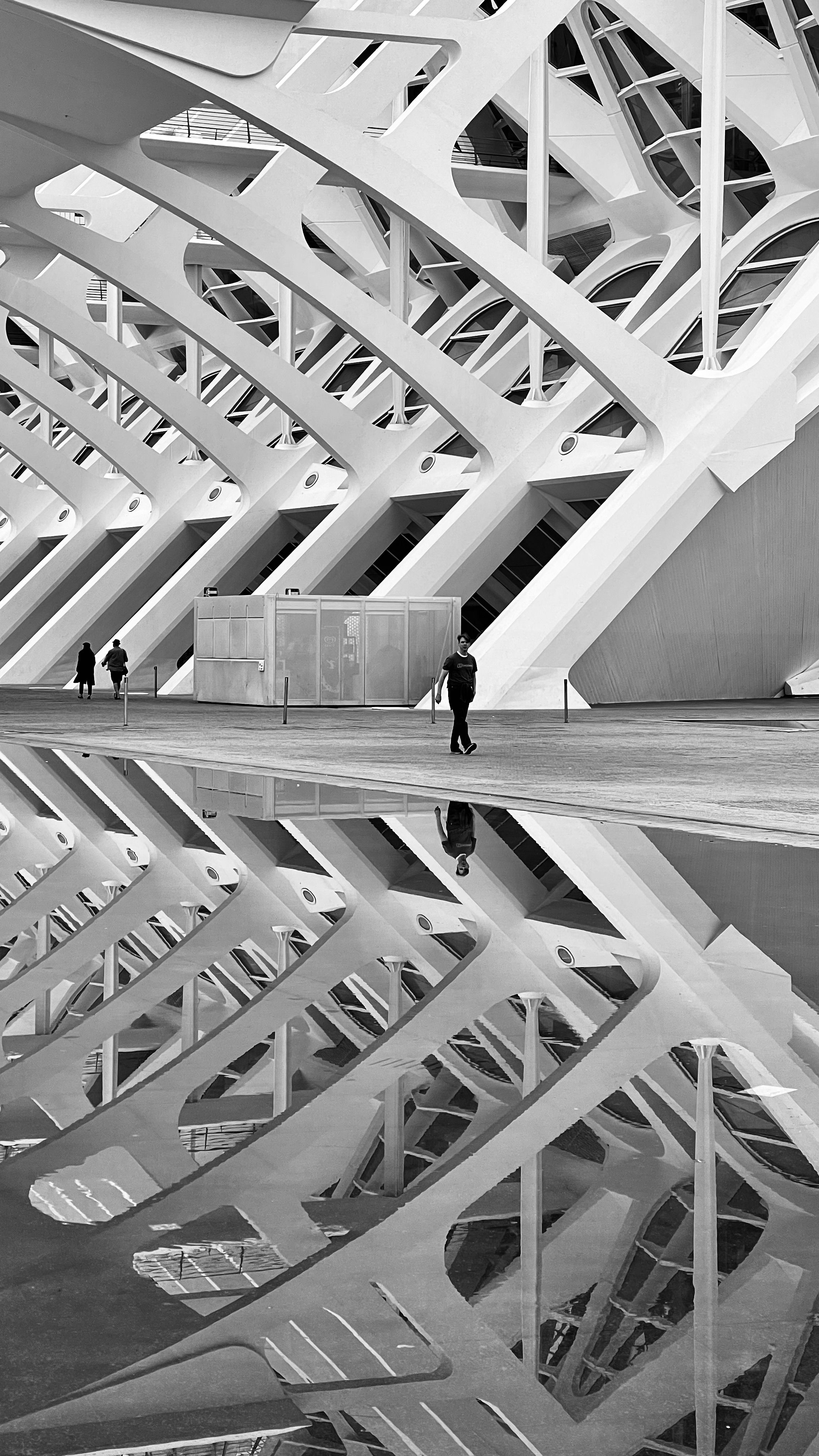 Black and white image of ultra-modern architecture with striking reflections and people walking.
