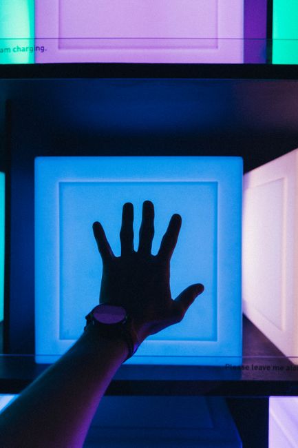 Silhouette of a hand reaching toward a glowing blue backlit modern art installation.